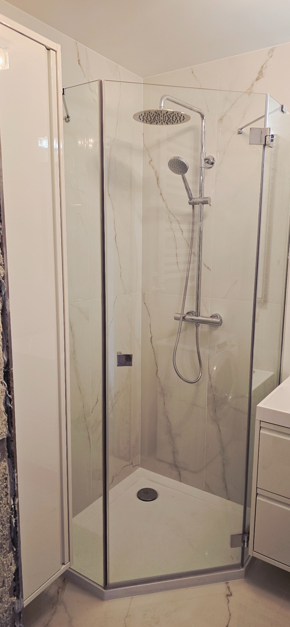 Nowoczesna kabina prysznicowa z marmurowymi płytkami, chromowaną armaturą i szklanymi drzwiami, widok z przodu, jasne oświetlenie.