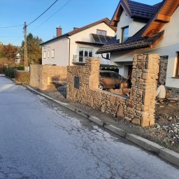 LUX-HAUS - Kamienna zabudowa ogrodzenia posesji z widocznym numerem domu, samochodem na podjeździe i pracującym mężczyzną w tle.