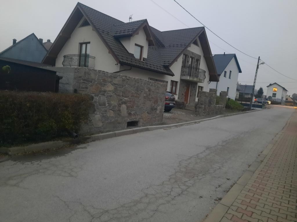 Dwupiętrowy dom z balkonami i kamiennym ogrodzeniem w pochmurny dzień, widok z ulicy.