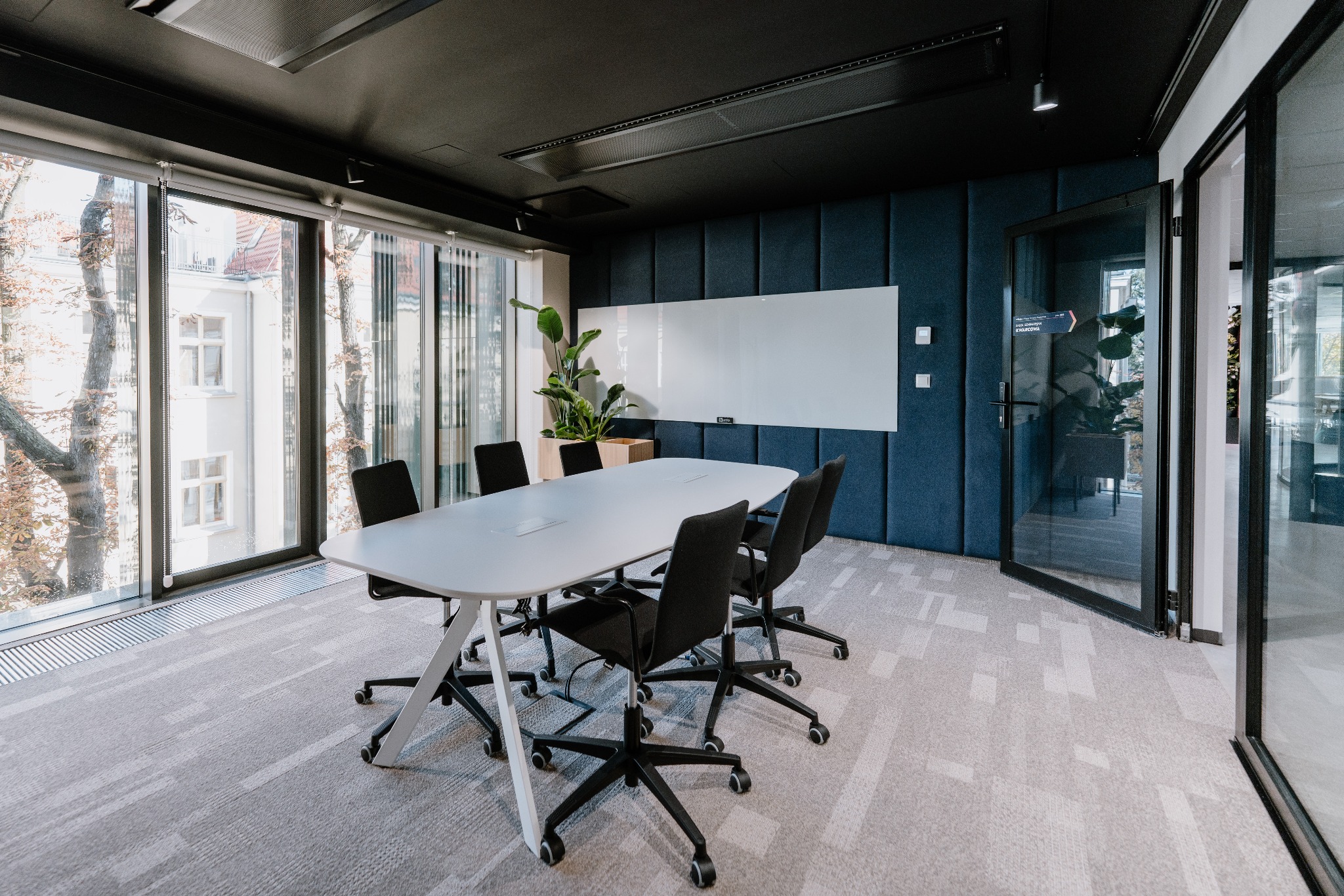 Nowoczesna sala konferencyjna we Wrocławiu z dużym oknem, białym stołem i krzesłami na kółkach, z widokiem na budynek po drugiej stronie ulicy.