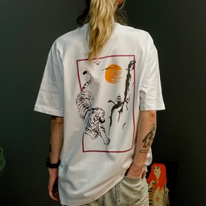 Biała koszulka z nadrukiem tygrysa, pagody i wschodzącego słońca na plecach osoby stojącej tyłem.