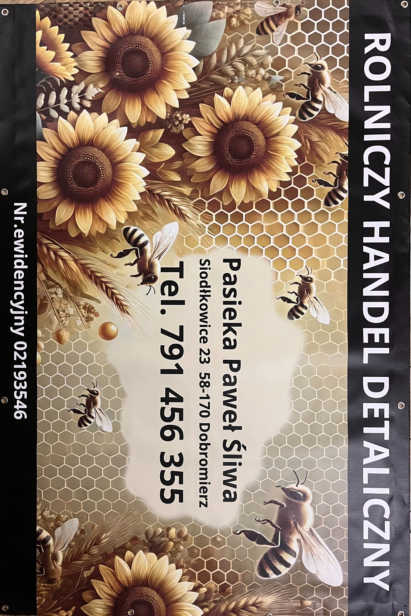 Baner reklamowy pasieki z motywem słoneczników i pszczół, wykonany w Udaninie. Wyraźny numer telefonu i adres, odporny na warunki atmosferyczne.