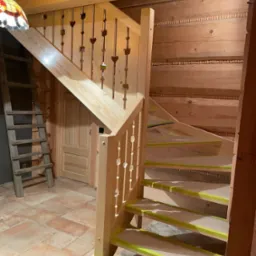 Drewniane schody w stylu góralskim z balustradą z wyciętymi sercami, zabezpieczone taśmą malarską przed wykończeniem. W tle ściany i sufit z rzeźbionego drewna.