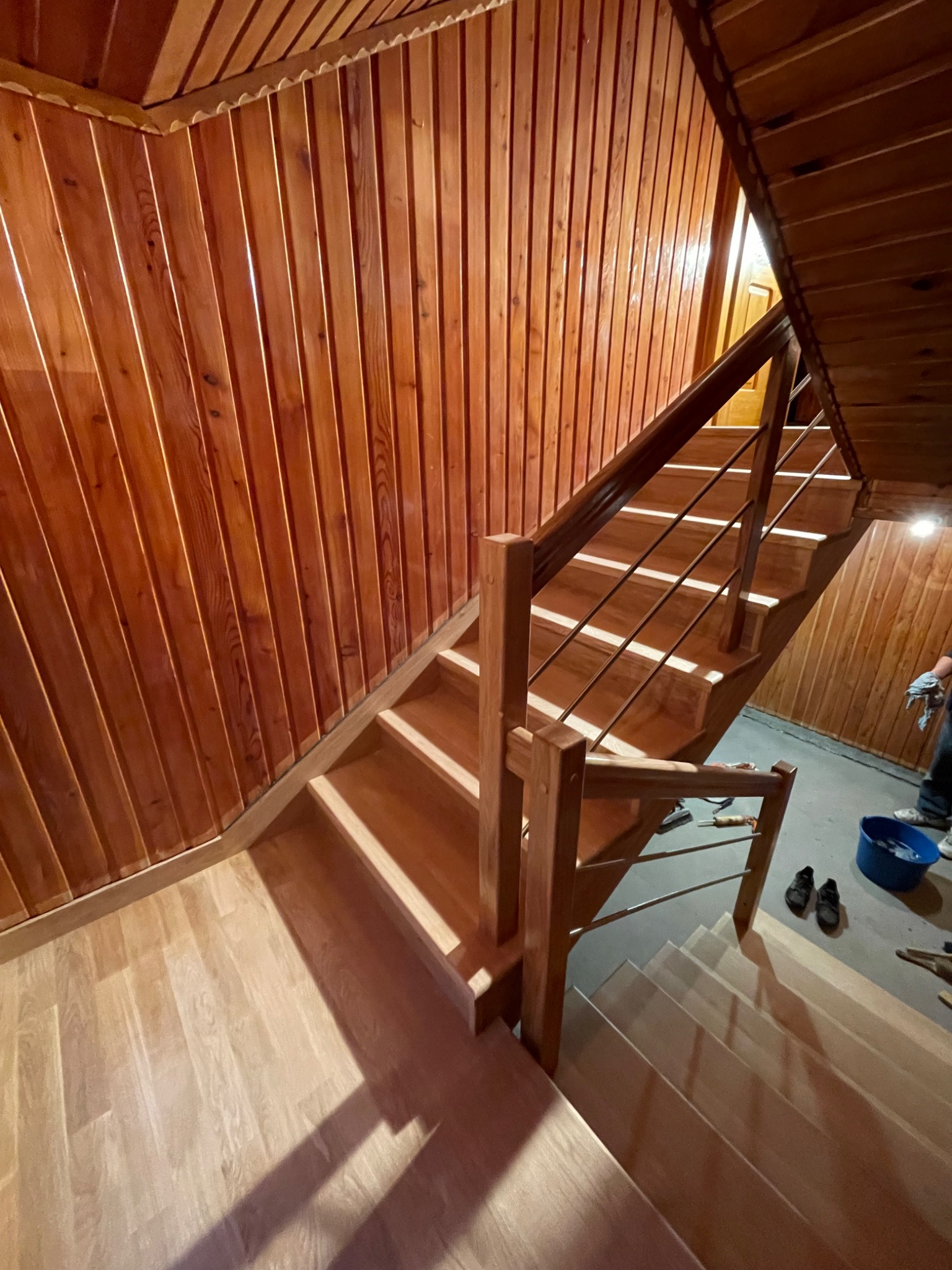 Drewniane schody z metalową balustradą wewnątrz domu, wykończone boazerią. Widoczne narzędzia i wiadro, sugerujące świeży montaż.