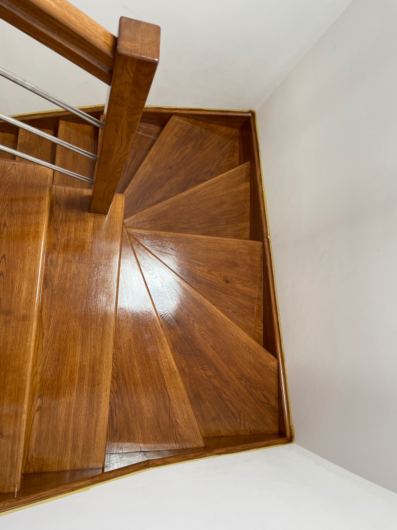 Wysoki kąt na spiralne schody drewniane z metalową balustradą. Ciepłe oświetlenie podkreśla lakierowane wykończenie stopni.