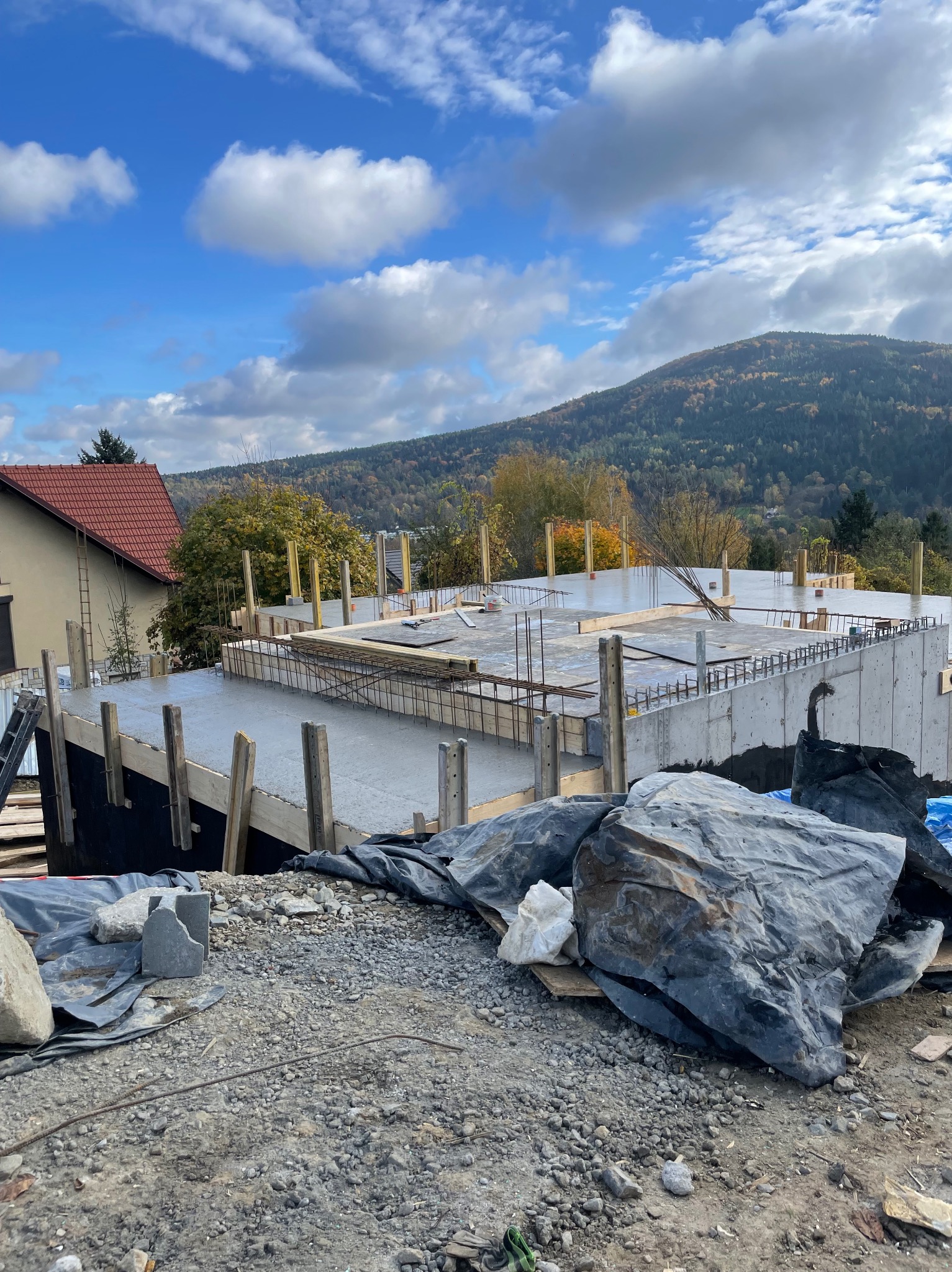 Wylany beton na stropie budynku w trakcie budowy, widoczne zbrojenia i szalunki. W tle góra i błękitne niebo z chmurami.