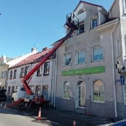 GNHome - Pracownik na podnośniku koszowym, w trakcie pracy przy elewacji budynku z widocznymi szyldami reklamowymi, na tle zabudowy miejskiej.