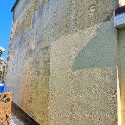 GNHome - Fragment elewacji budynku w trakcie czyszczenia. Widoczna różnica między umytą a zabrudzoną powierzchnią. Ujęcie z dołu, podkreślające wysokość ściany.