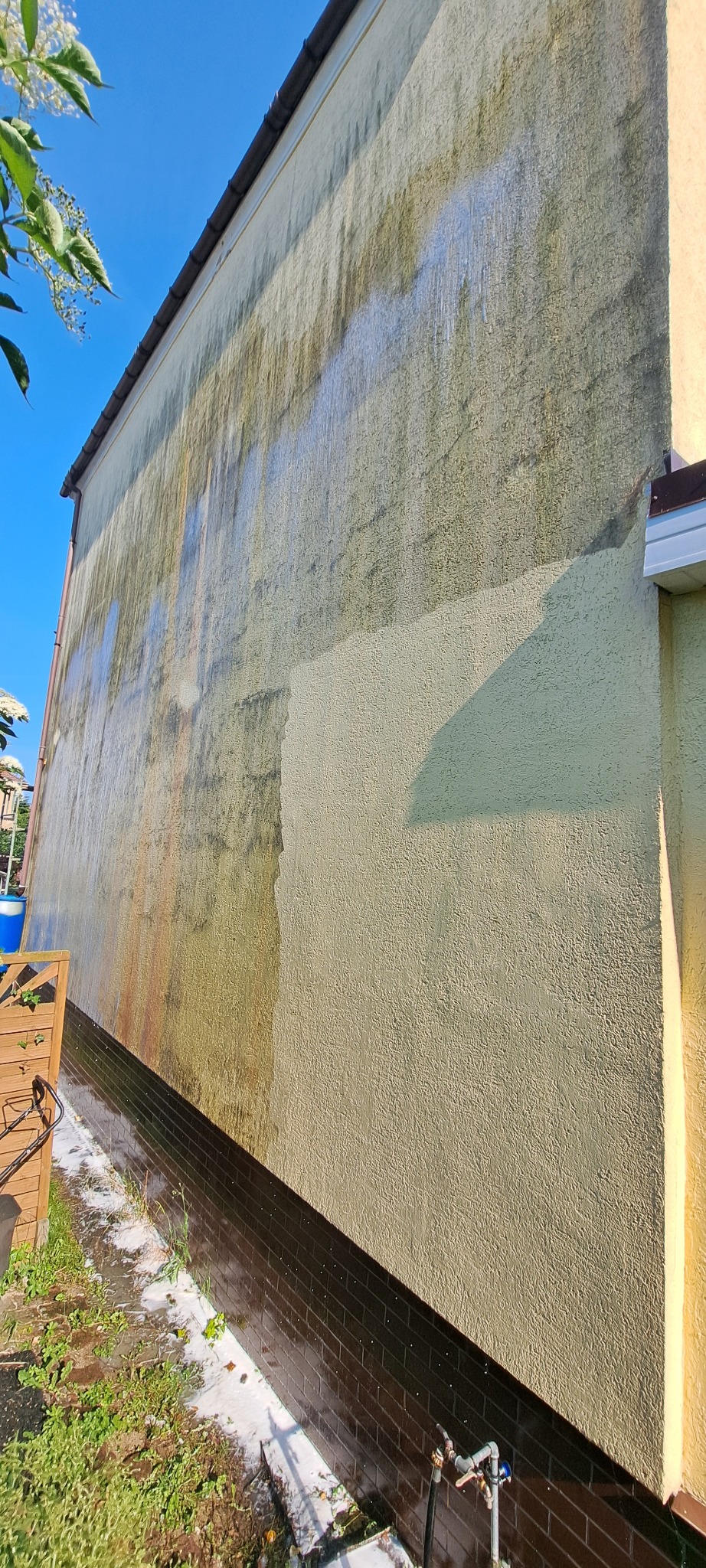 Fragment elewacji budynku w trakcie czyszczenia. Widoczna różnica między umytą a zabrudzoną powierzchnią. Ujęcie z dołu, podkreślające wysokość ściany.