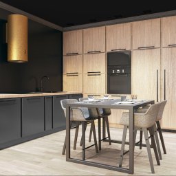MASS STUDIO - Nowoczesna kuchnia z drewnianymi szafkami, czarnymi blatami i złotym okapem cylindrycznym. Stół barowy z czterema krzesłami i nakryciem stoi na pierwszym planie.
