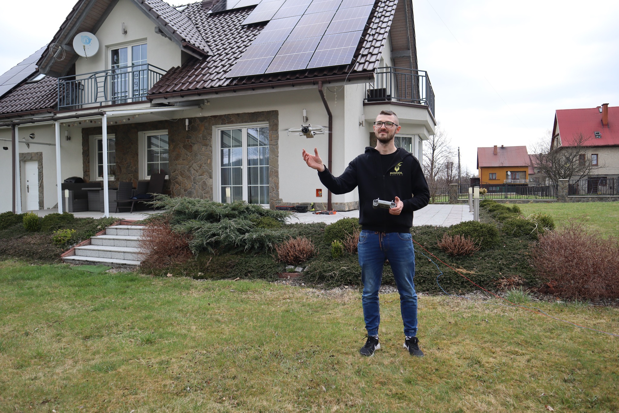 Mężczyzna z dronem inspekcyjnym na tle domu z panelami słonecznymi na dachu. Wykorzystanie drona do inspekcji instalacji elektrycznych.