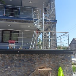 Maciek dropinski - Montaż zewnętrznej balustrady nierdzewnej na balkonie z spiralnymi schodami, widoczny pracownik na schodach i narzędzia pracy.