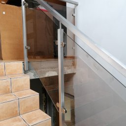 Maciek dropinski - Szklana balustrada z metalowymi słupkami zamocowana na schodach wyłożonych terakotą, widok z dołu na górę.