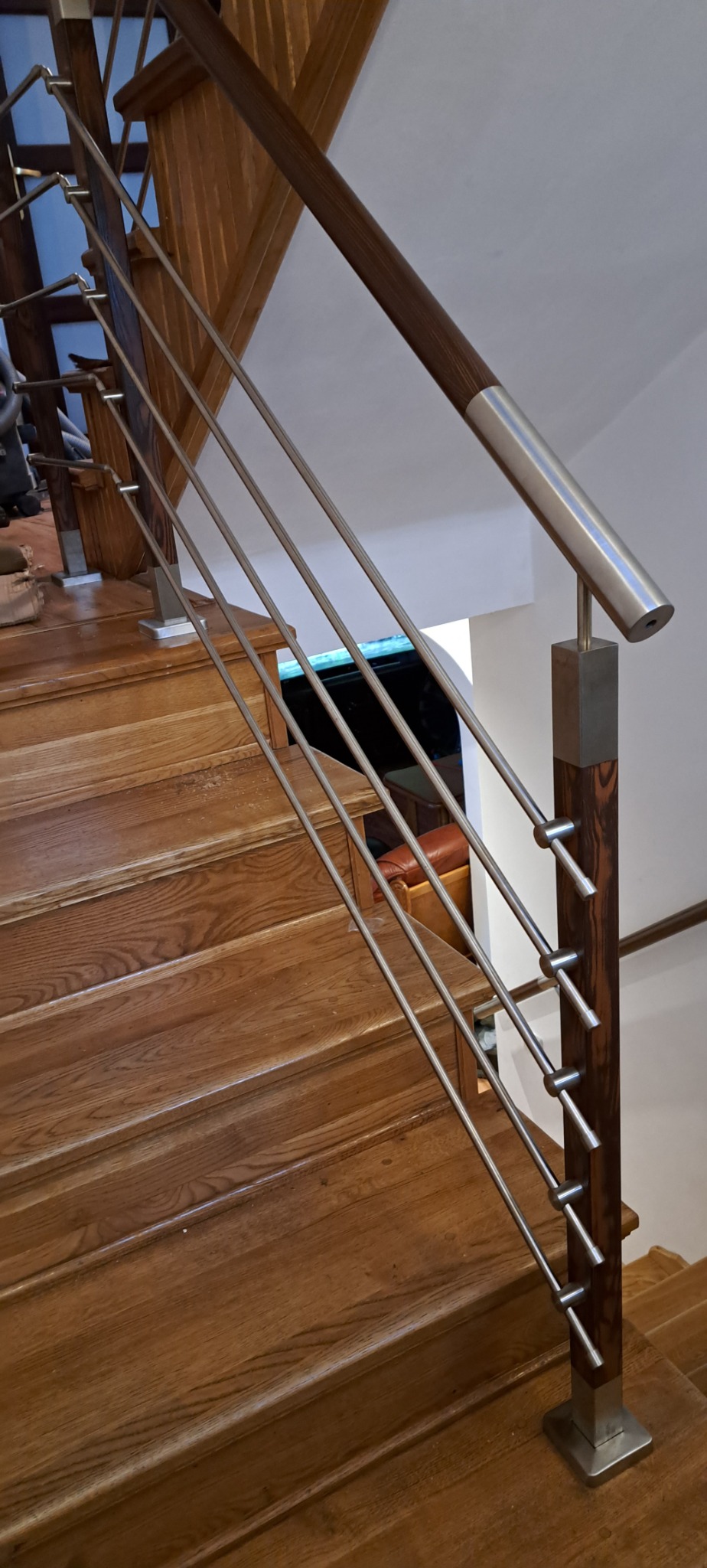 Drewniane schody z nowoczesną balustradą z poziomych, cienkich prętów i drewnianą poręczą z metalowymi zakończeniami.