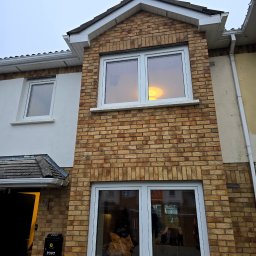 FENBRO SPÓŁKA Z OGRANICZONĄ ODPOWIEDZIALNOŚCIĄ - Dwukondygnacyjny dom z cegły z białymi oknami, skrzynka pocztowa z motywem słonecznika przy wejściu.