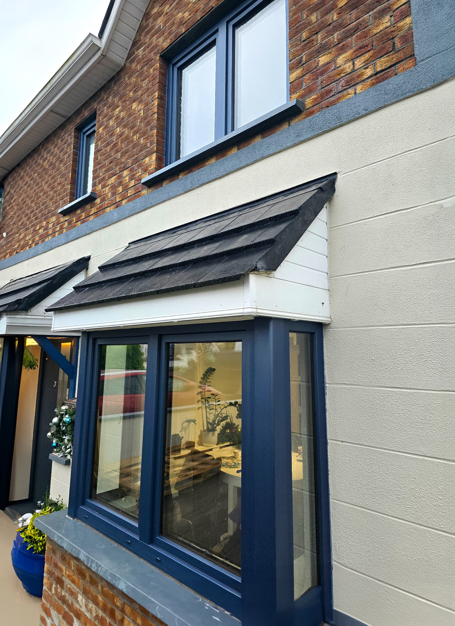 Wystający okap nad oknem PCV w kolorze antracytowym, z widoczną teksturą ściany zewnętrznej i elementami dekoracyjnymi wewnątrz pomieszczenia.