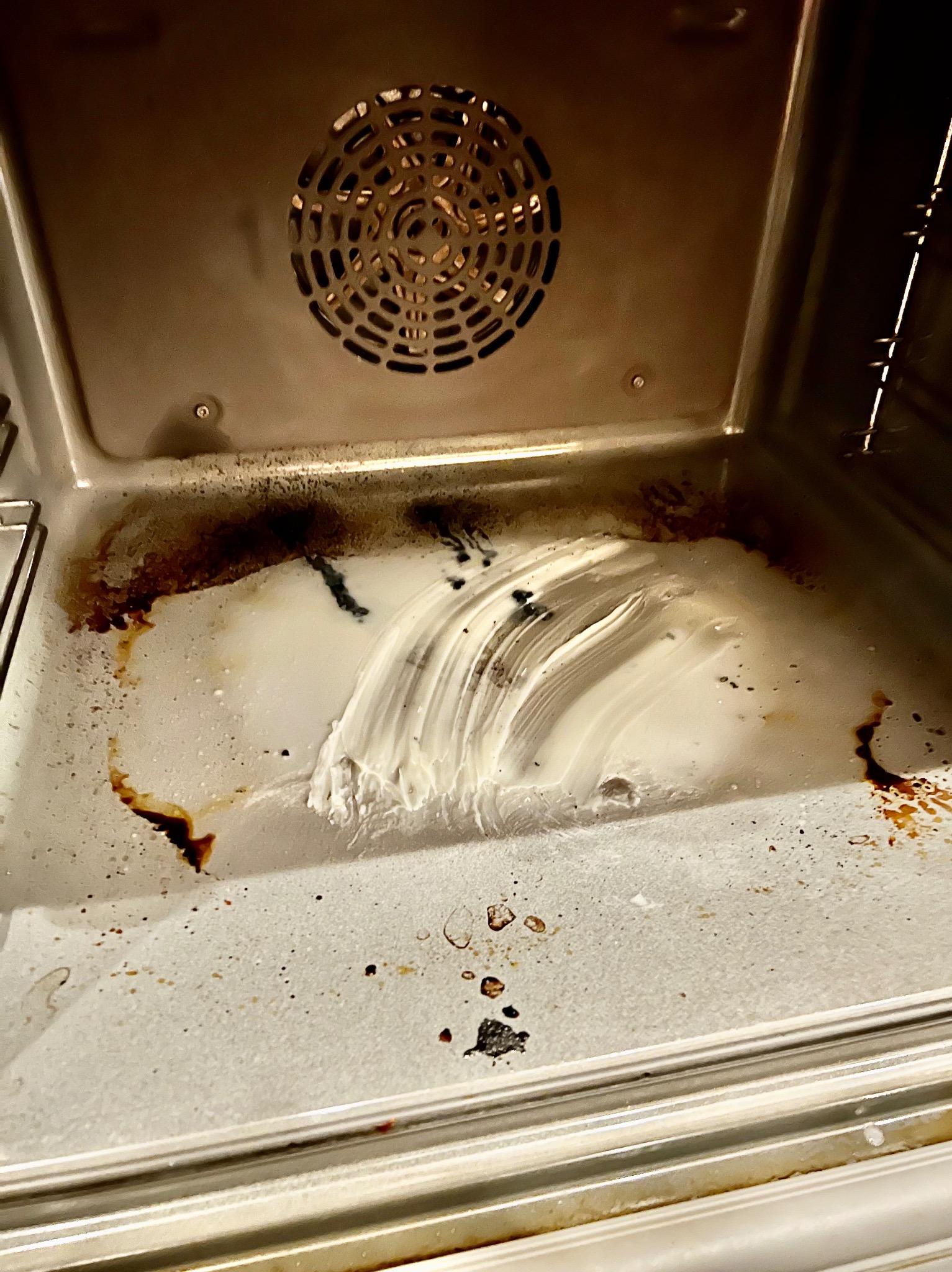 Wnętrze brudnego piekarnika z resztkami jedzenia i nałożonym środkiem czyszczącym przed procesem sprzątania.