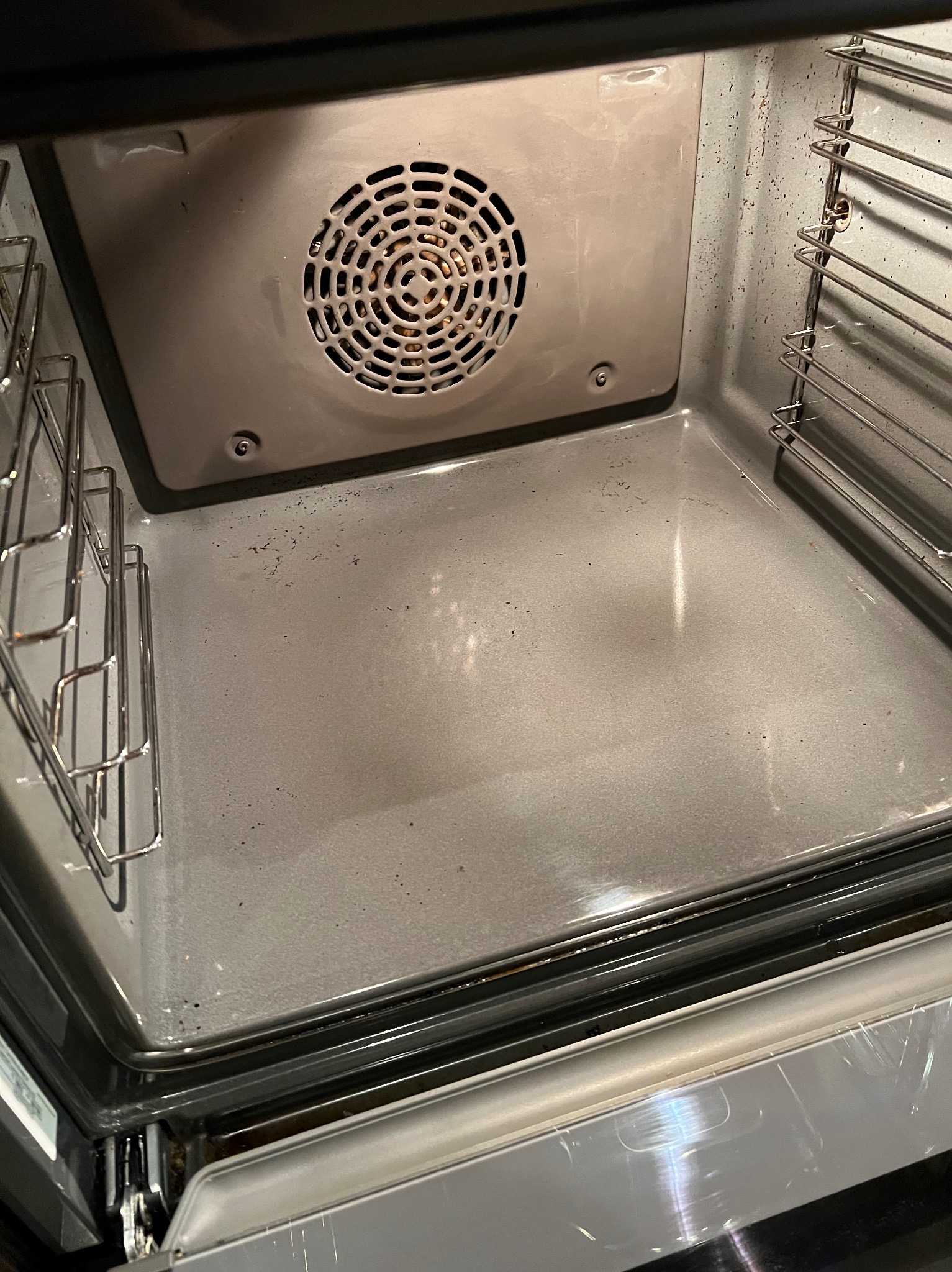 Wnętrze brudnego piekarnika z widocznymi przypaleniami i resztkami jedzenia na dnie oraz na ściankach, kratki w piekarniku również zabrudzone.