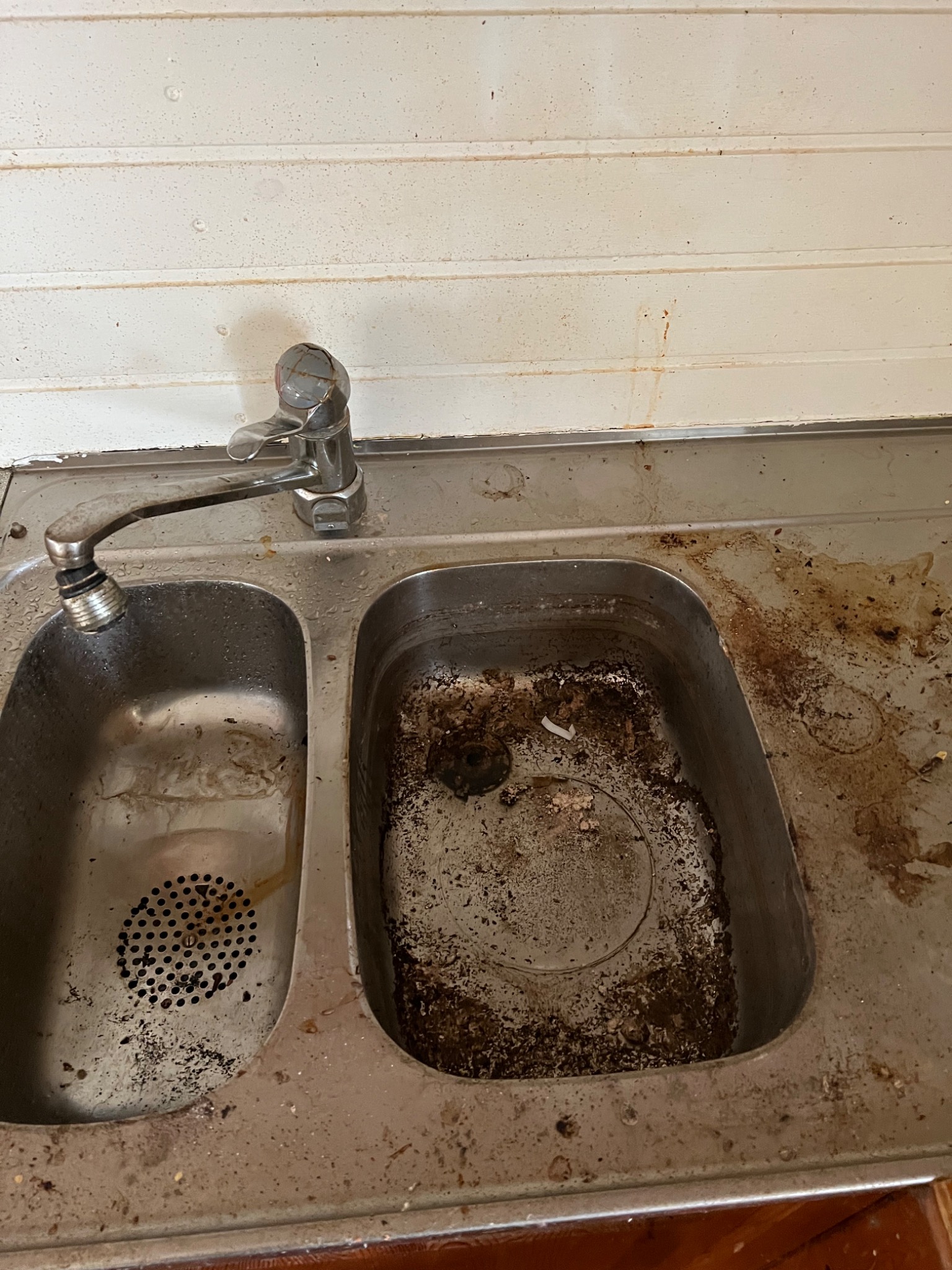 Bardzo brudny, dwukomorowy zlew kuchenny ze stali nierdzewnej przed czyszczeniem, widoczne zaschnięte resztki jedzenia i zabrudzenia na ściankach i dnie komór.