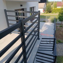 Inox4home - Nowoczesna, pozioma balustrada metalowa w kolorze grafitowym, zamontowana na balkonie domu jednorodzinnego. Widoczne narzędzia montażowe na podłodze balkonu.