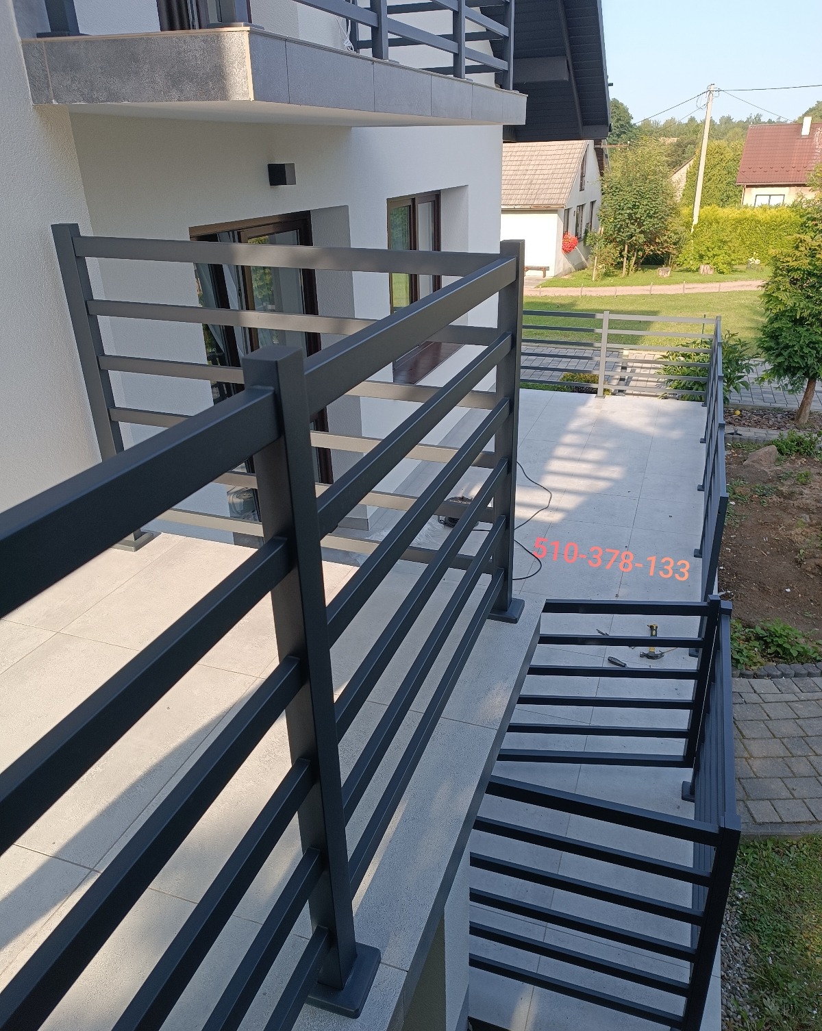 Nowoczesna, pozioma balustrada metalowa w kolorze grafitowym, zamontowana na balkonie domu jednorodzinnego. Widoczne narzędzia montażowe na podłodze balkonu.