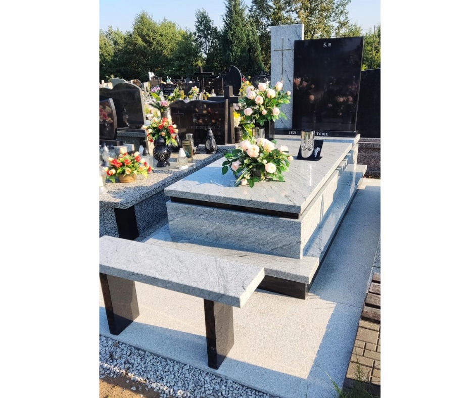 Jasnoszary granitowy pomnik z czarną tablicą nagrobną i bukietem kwiatów w wazonie, na cmentarzu.
