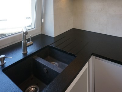 Czarny, teksturowany blat kuchenny z wbudowanym zlewozmywakiem dwukomorowym i ociekaczem, widok z bliska na armaturę i dozownik mydła.