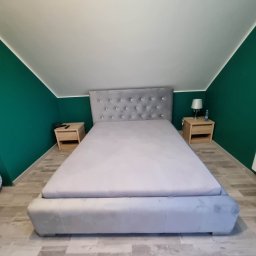 Tapicerstwo Izydorski - Szare tapicerowane łóżko z kryształkami na wezgłowiu w pokoju na poddaszu z zielonymi ścianami i drewnianymi szafkami nocnymi.