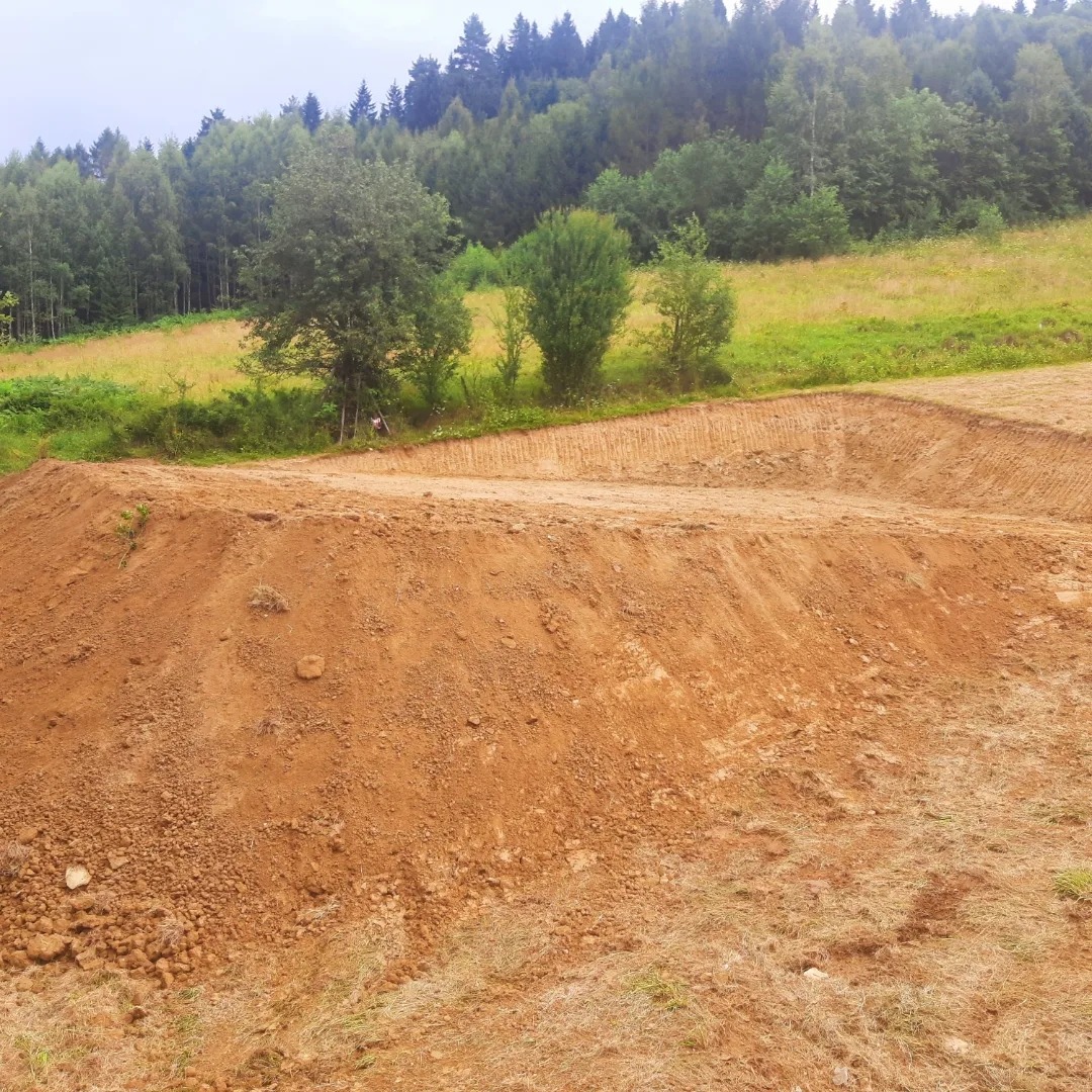 Uformowany teren z wykopaną ziemią pod przyszłą budowę na tle zielonego wzgórza z drzewami.