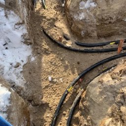 PRO TECH Tomasz Palkowski - Wykop z ułożonymi przewodami elektrycznymi w ziemi, widoczne oznaczenia na kablach i resztki śniegu na ścianach wykopu.