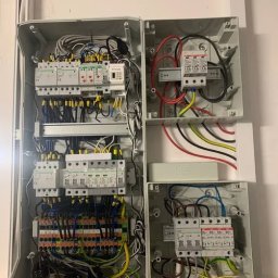 PRO TECH Tomasz Palkowski - Otwarta szafa elektryczna z widocznymi zabezpieczeniami przepięciowymi, bezpiecznikami i okablowaniem w kolorach: czerwonym, żółto-zielonym, czarnym i niebieskim. Na dole widoczne etykiety...