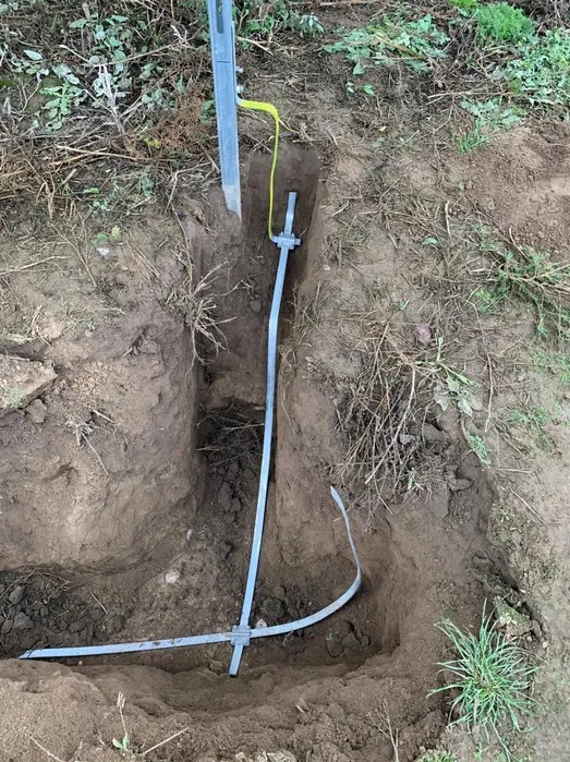 Instalacja uziomu pionowego z bednarką w wykopie ziemnym, widoczny przewód żółto-zielony.