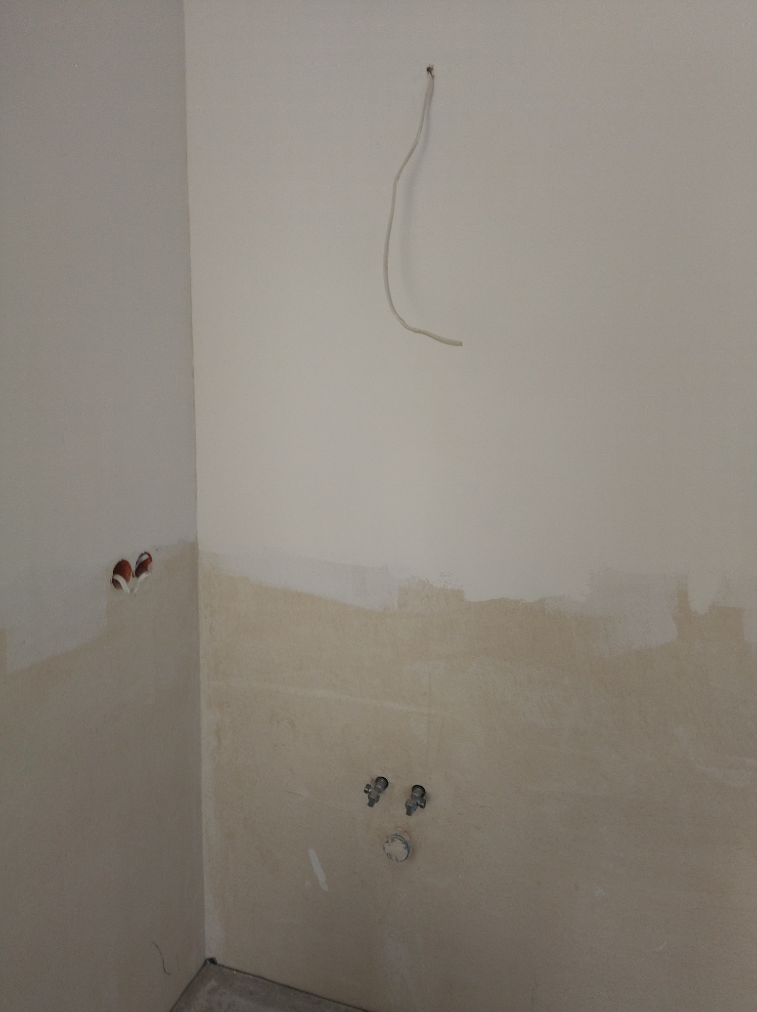 Ściana w trakcie remontu z wystającymi przewodami i rurami. Widoczne otwory pod gniazdka i instalacje wodne. Przygotowanie do wykończenia.