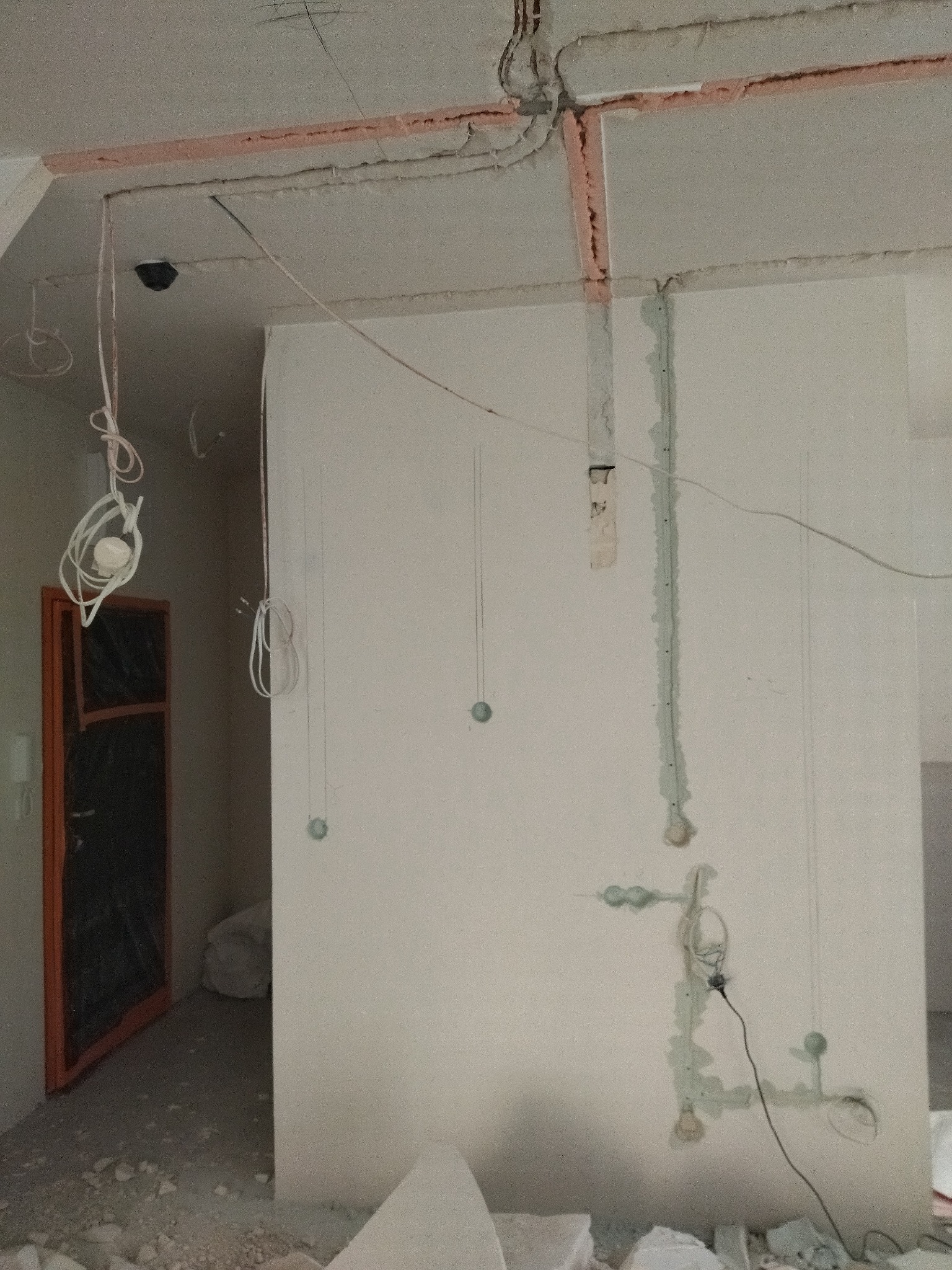 Instalacja elektryczna w trakcie remontu: kable wystające ze ścian i sufitu, przygotowane pod gniazdka i oświetlenie. Widoczne bruzdy wypełnione gipsem.