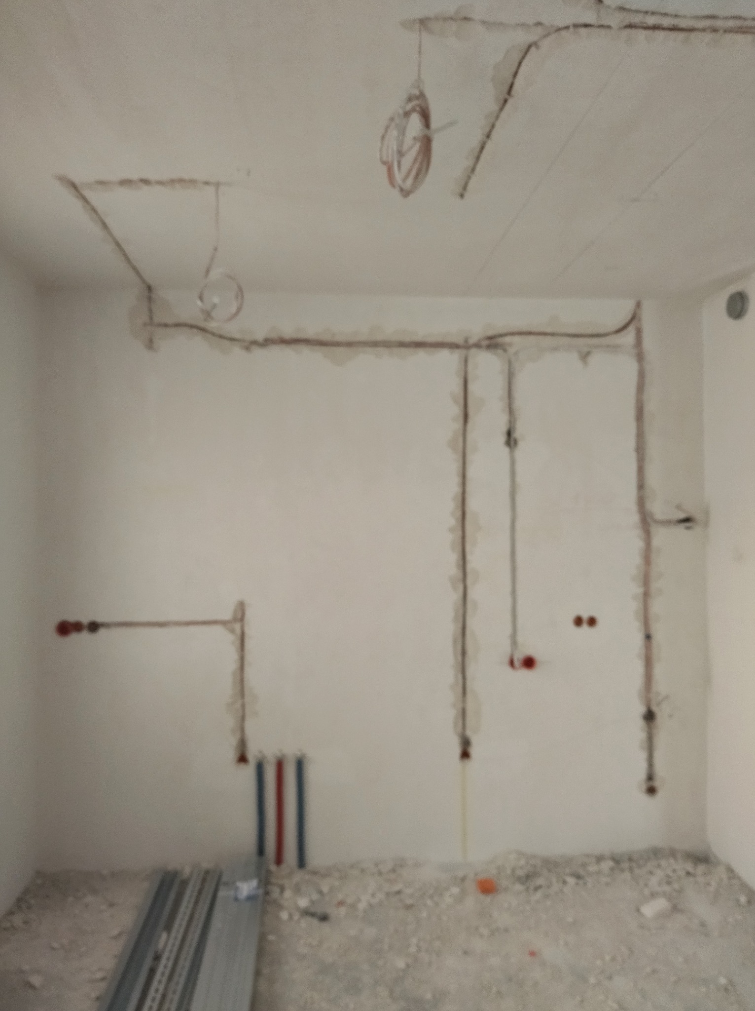 Wnętrze w trakcie prac instalacyjnych: kable elektryczne i rury wodne prowadzone po ścianach i suficie, widoczne puszki instalacyjne i elementy mocujące.