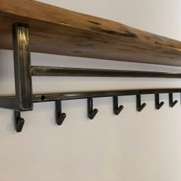 ELMAT Mateusz Ziętek - Półka ścienna z surowego drewna i metalową konstrukcją z wieszakami, minimalistyczny design na białym tle.