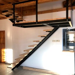 ELMAT Mateusz Ziętek - Nowoczesne schody z czarną metalową konstrukcją i drewnianymi stopniami prowadzące na antresolę, widoczne surowe drewno na podłodze i drewniany sufit.