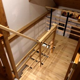 ELMAT Mateusz Ziętek - Drewniane schody i balustrada w jasnym odcieniu drewna, widok z góry na antresolę w poddaszu, minimalistyczny design z elementami metalowymi.