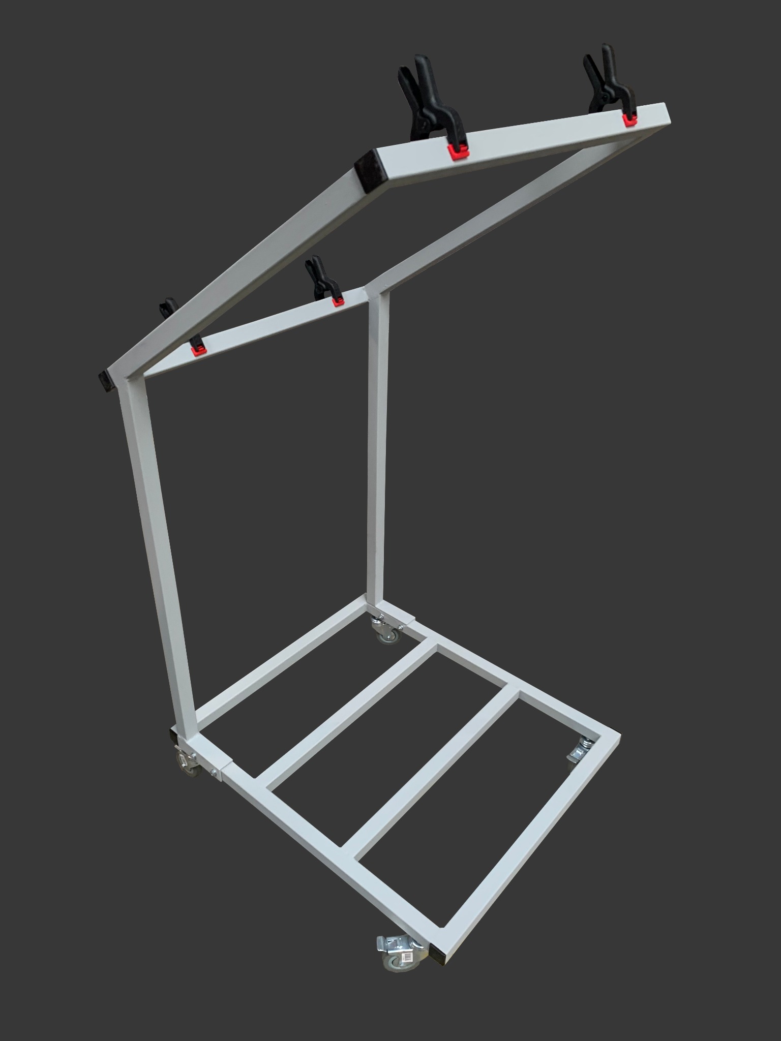 Metalowa konstrukcja na kółkach w kształcie odwróconej litery L, z czarnymi zaciskami i czerwonymi akcentami, na szarym tle.