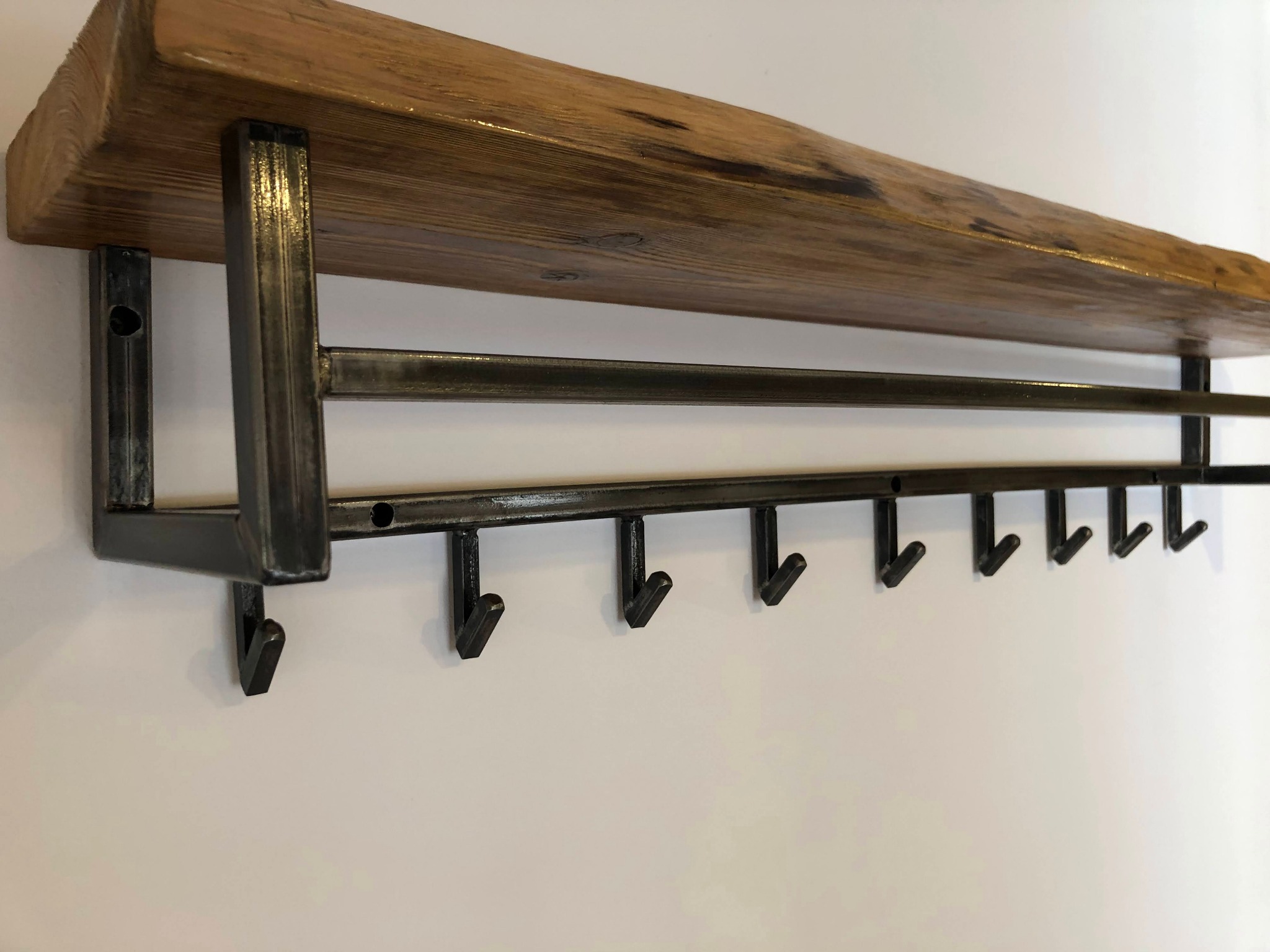 Półka ścienna z surowego drewna i metalową konstrukcją z wieszakami, minimalistyczny design na białym tle.