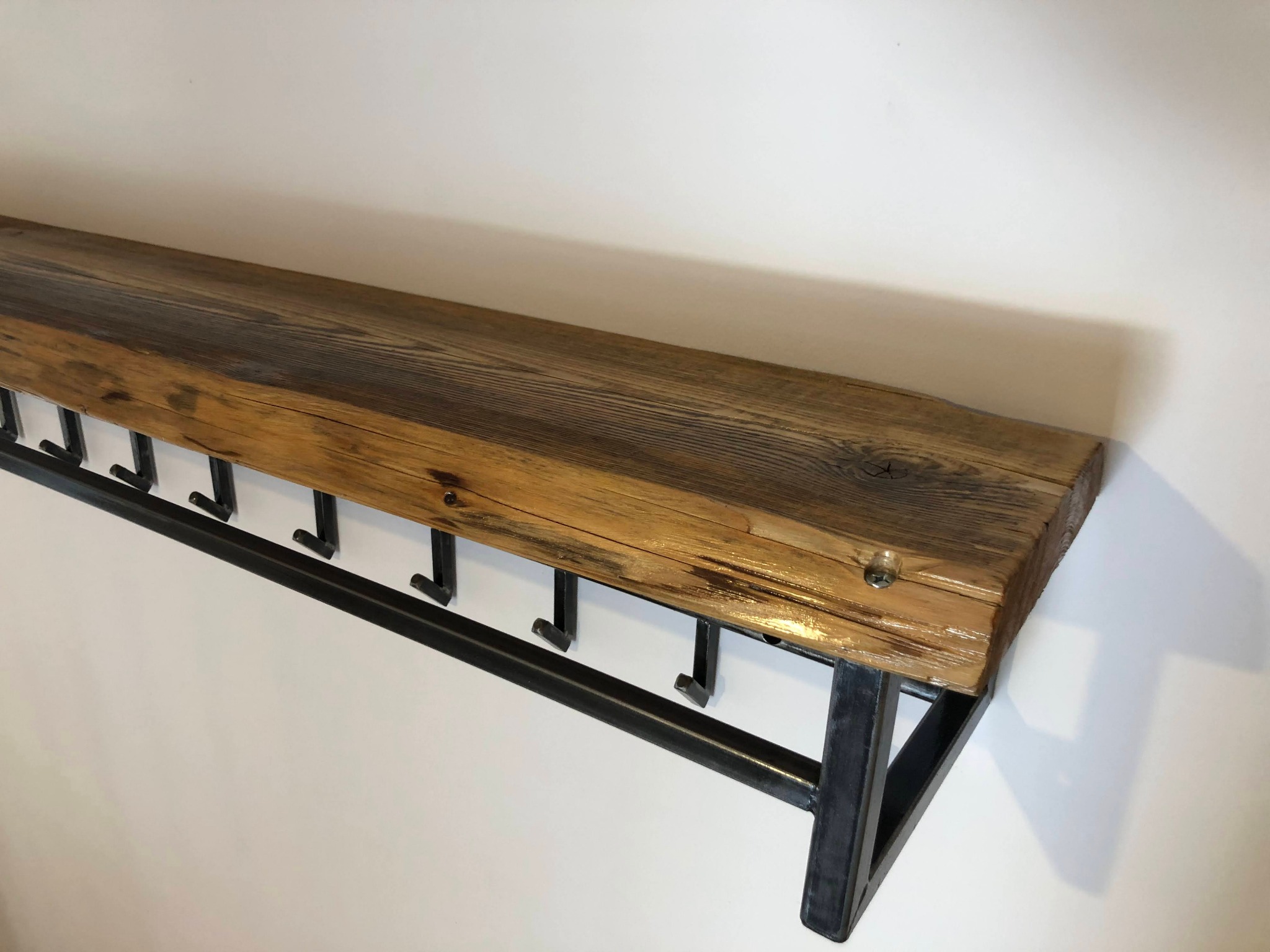 Półka ścienna z surowego drewna mocowana do metalowej ramy z haczykami na ubrania, widok z dołu.