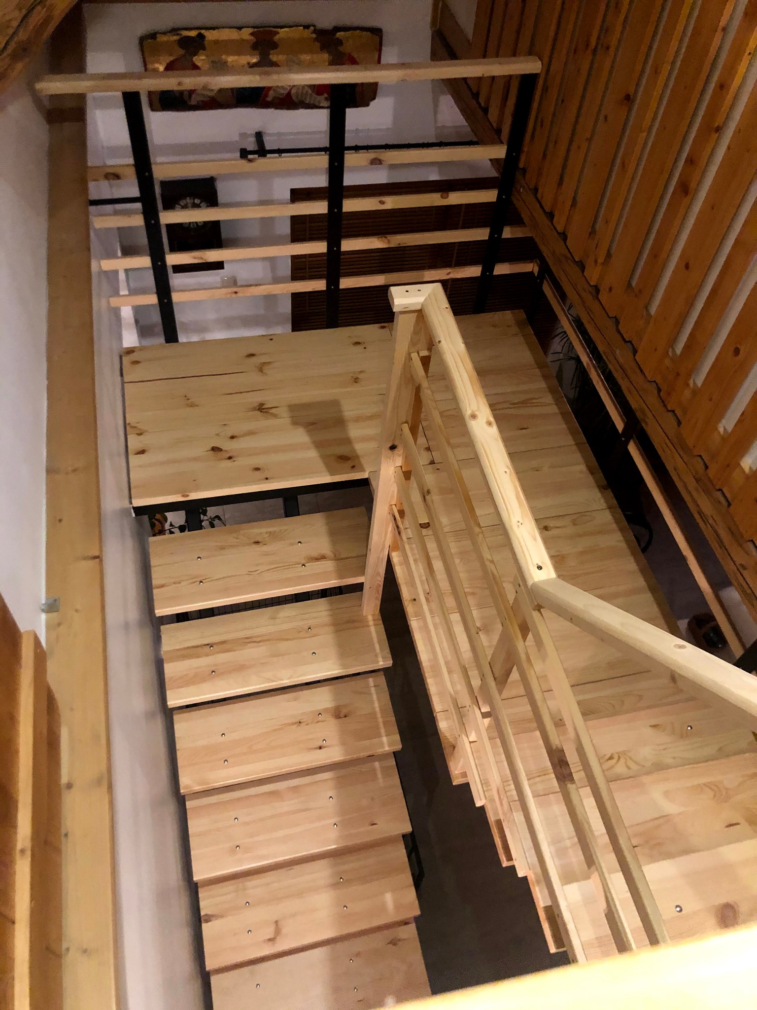 Drewniane schody z metalową konstrukcją nośną, widok z góry na stopnie i poręcze z jasnego drewna w surowym wykończeniu.