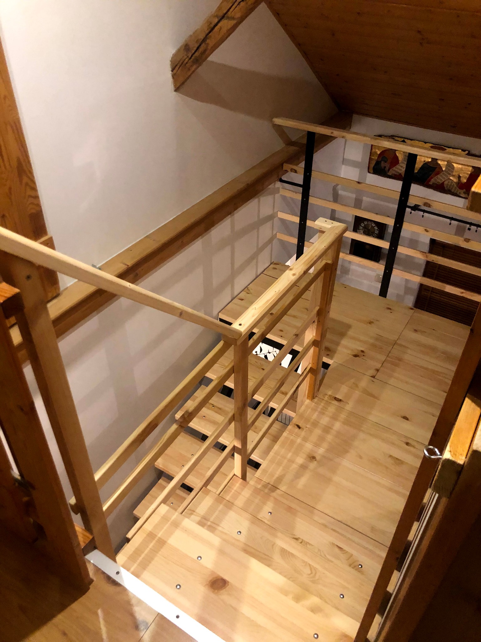 Drewniane schody i balustrada w jasnym odcieniu drewna, widok z góry na antresolę w poddaszu, minimalistyczny design z elementami metalowymi.