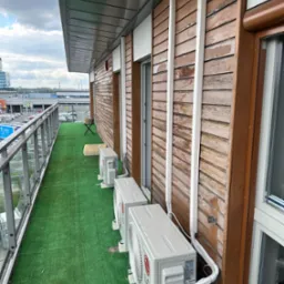 Balkon z trzema zewnętrznymi jednostkami klimatyzacji LG, widok na miasto w tle, sztuczna trawa na podłodze.