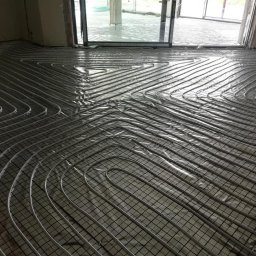 USŁUGI INSTALACYJNE KRYSTIAN SŁOWIOK - Montaż ogrzewania podłogowego w Zabrzu: rury grzewcze ułożone na siatce, przygotowane do zalania wylewką, widok na okno tarasowe.