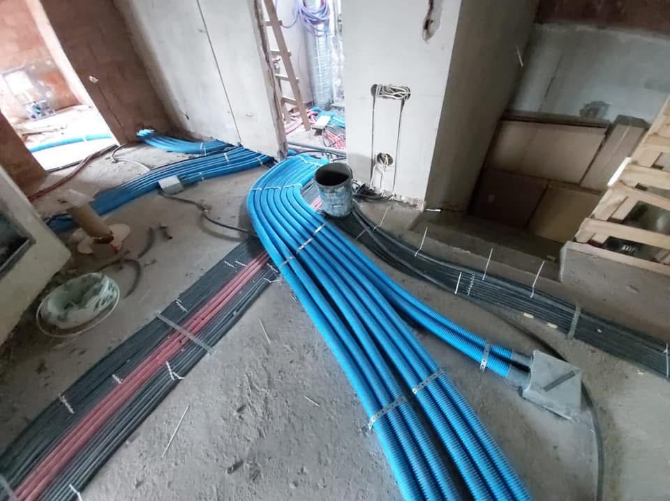 Instalacja rur karbowanych w kolorze niebieskim i przewodów elektrycznych w surowym stanie, z widoczną drabiną i puszkami instalacyjnymi w tle.