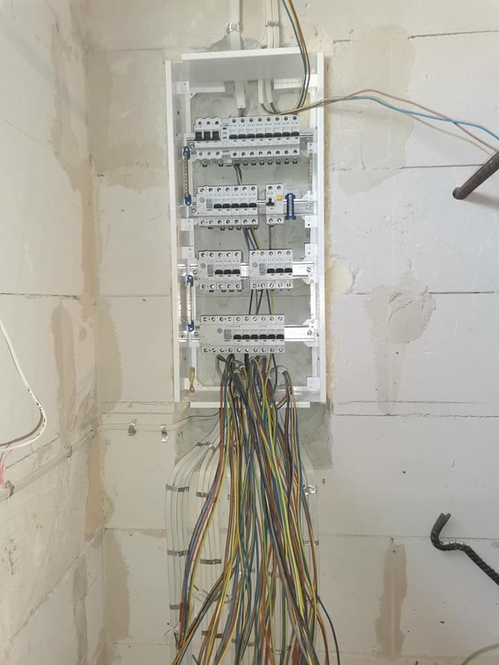 Szafa rozdzielcza w trakcie montażu, z licznymi przewodami wychodzącymi dołem, zamontowana na surowej ścianie z betonu komórkowego.