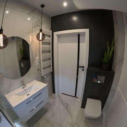 Daniel P - Nowoczesna łazienka z umywalką na szafce, okrągłym lustrem, grzejnikiem drabinkowym i wiszącymi lampami z żarówkami Edisona, wykończona płytkami imitującymi marmur i ciemnoszarą okładziną.