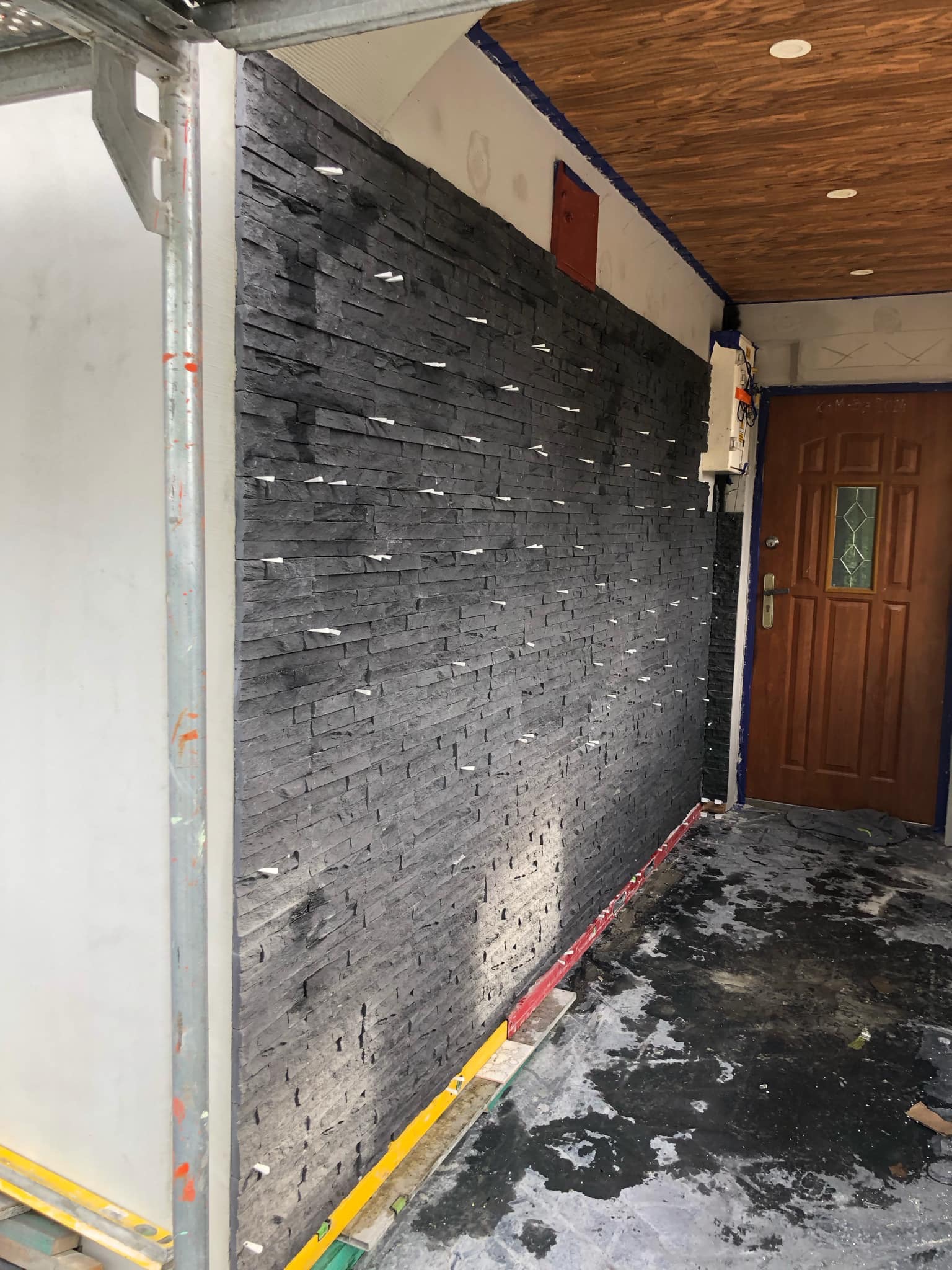 Montaż okładziny z imitacji kamienia na elewacji budynku, widoczne białe krzyżyki dystansowe, rusztowanie i częściowo zabezpieczona podłoga.