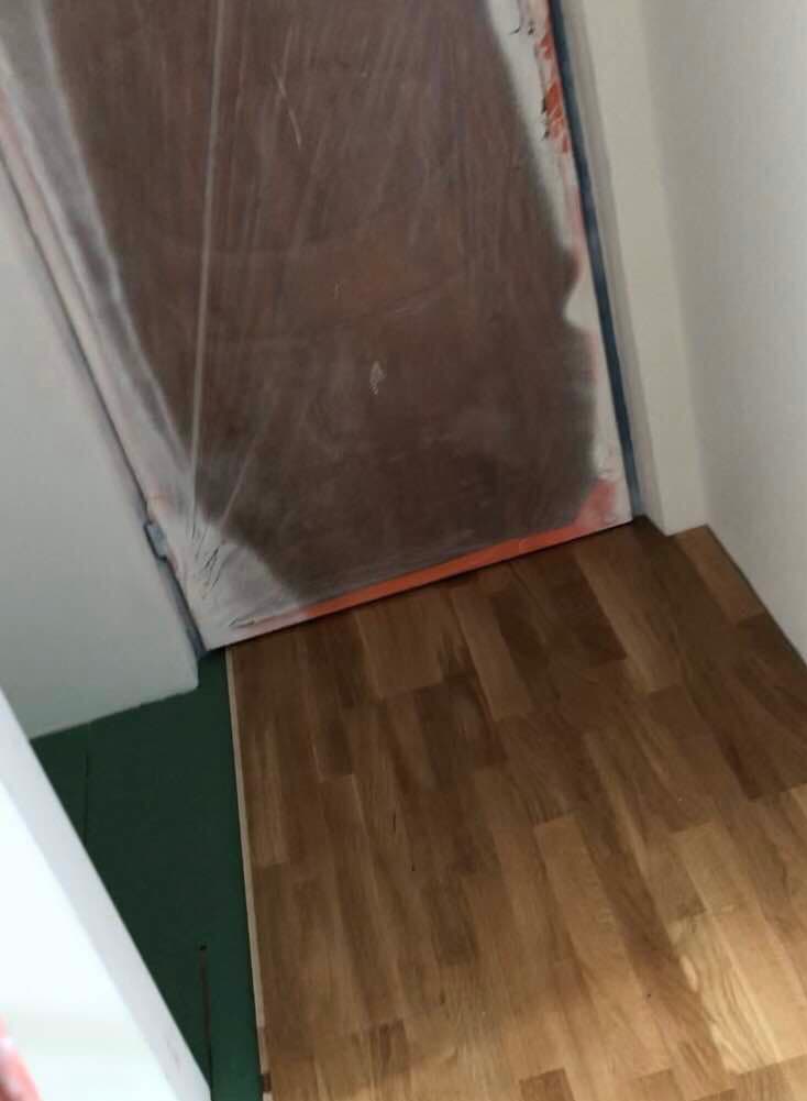 Fragment pokoju z nowo ułożonymi panelami podłogowymi, zabezpieczone drzwi folią malarską, widoczna zielona podkładka pod panele.